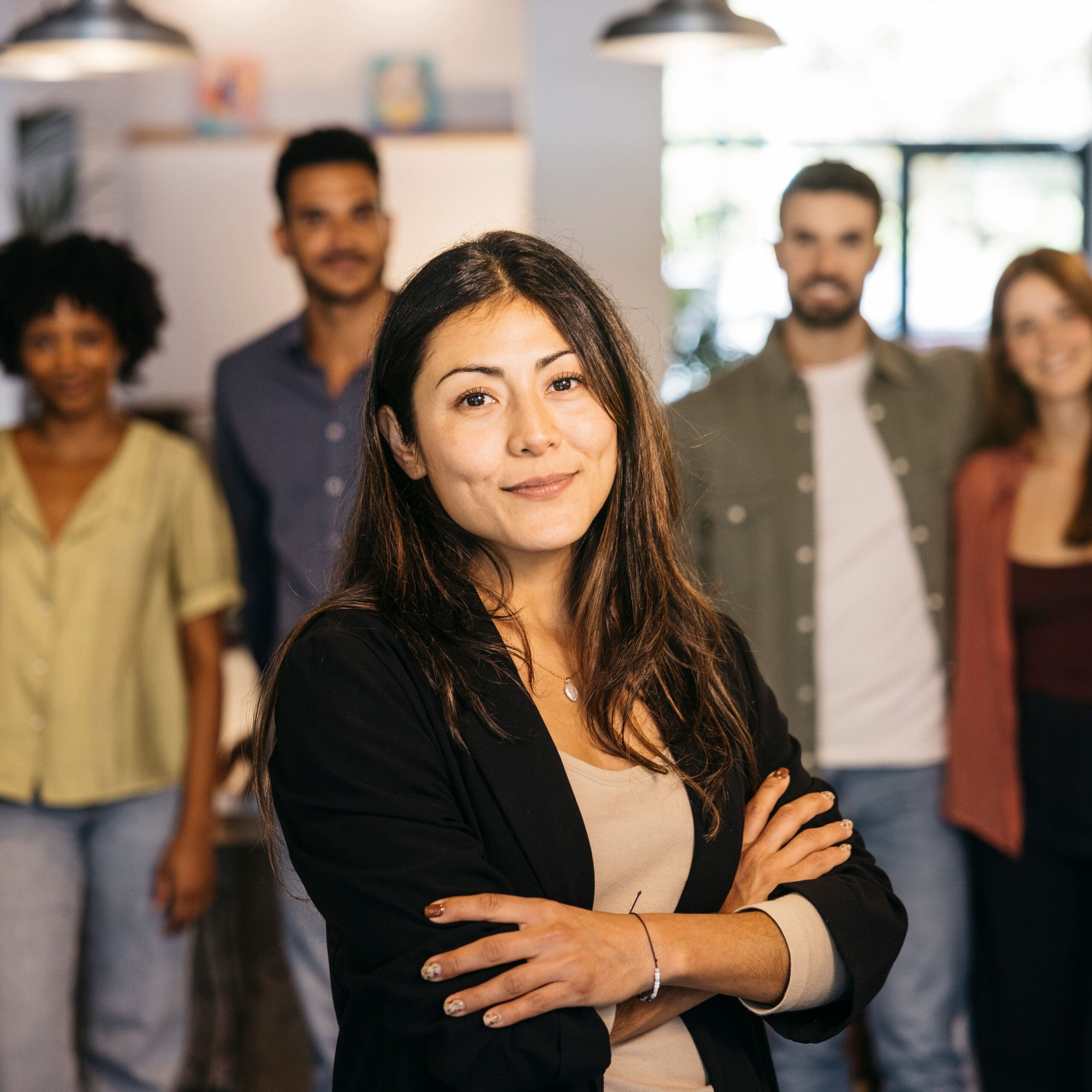 Confident female leader with arms crossed standing in front of her diverse business team